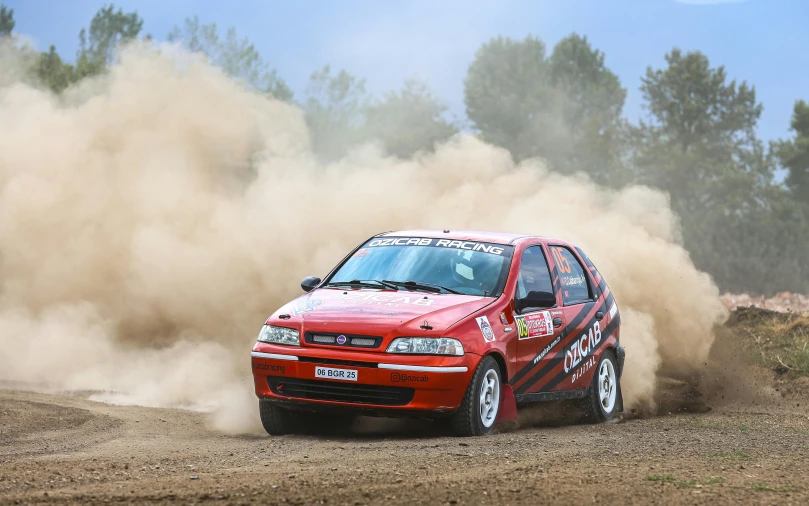 a red car with an all weather cover driving down a dirt road