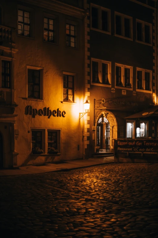 a stone street has an open - fronted building lit up at night