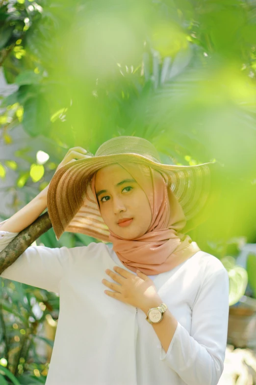 a woman in white shirt and straw hat posing by a tree