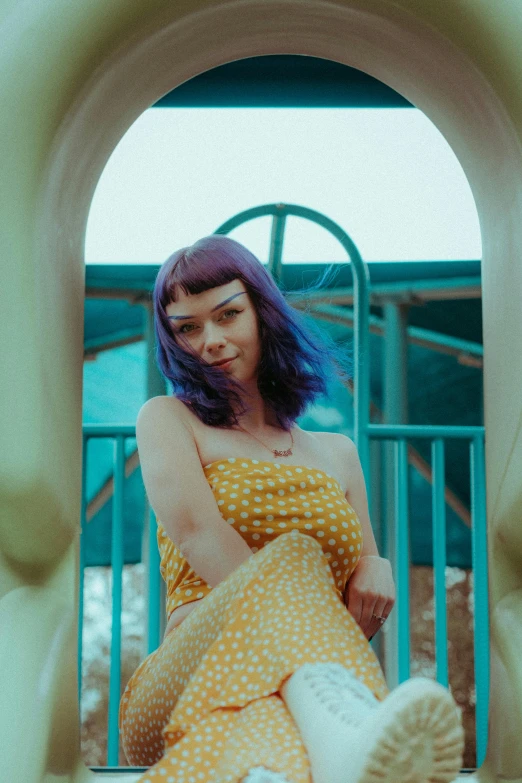 a woman with purple hair and yellow polka dots sitting in a blue playground swing