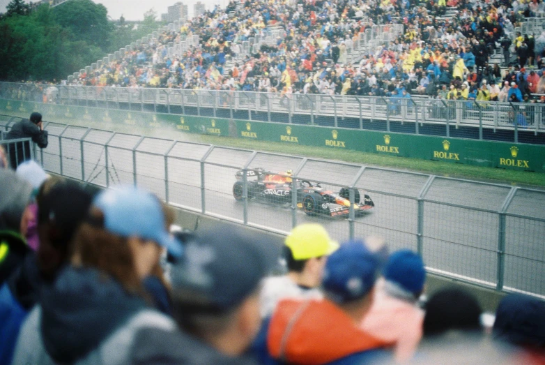 a crowd is watching the race during a rain soaked track