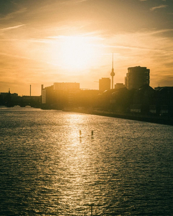 an orange and yellow sky reflecting on water in a city