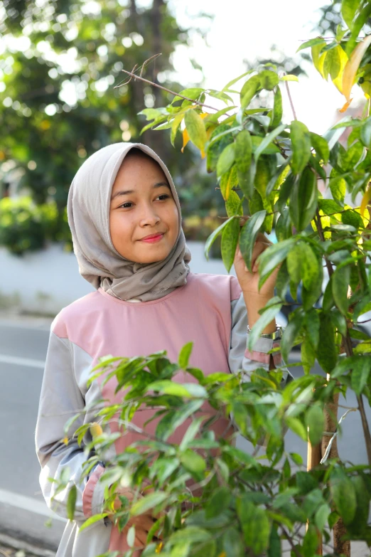 girl with a hijab holding green leaves on the tree
