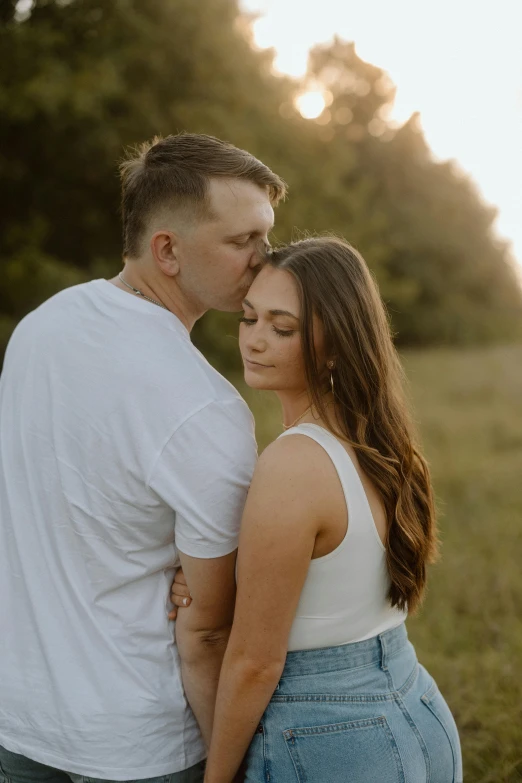 a couple cuddles as the sun rises over their heads in a field