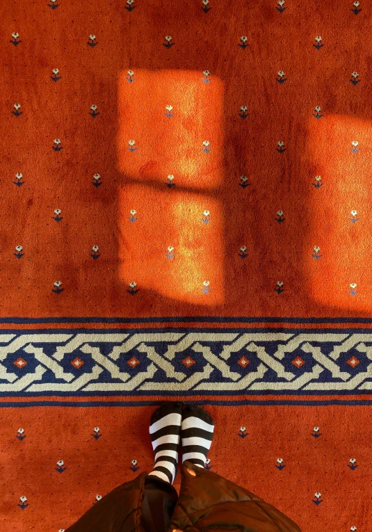 a persons feet on an orange rug with blue and white stripes