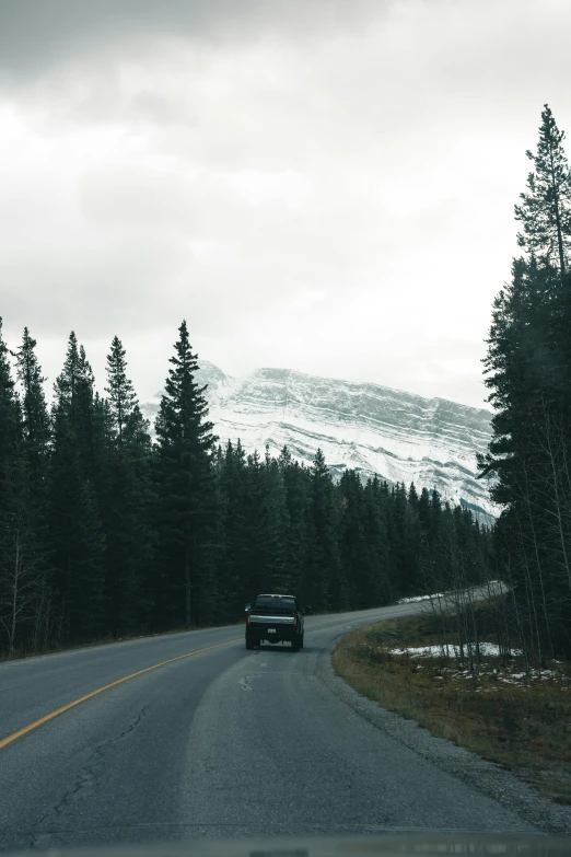 a truck driving down the middle of a road in the woods