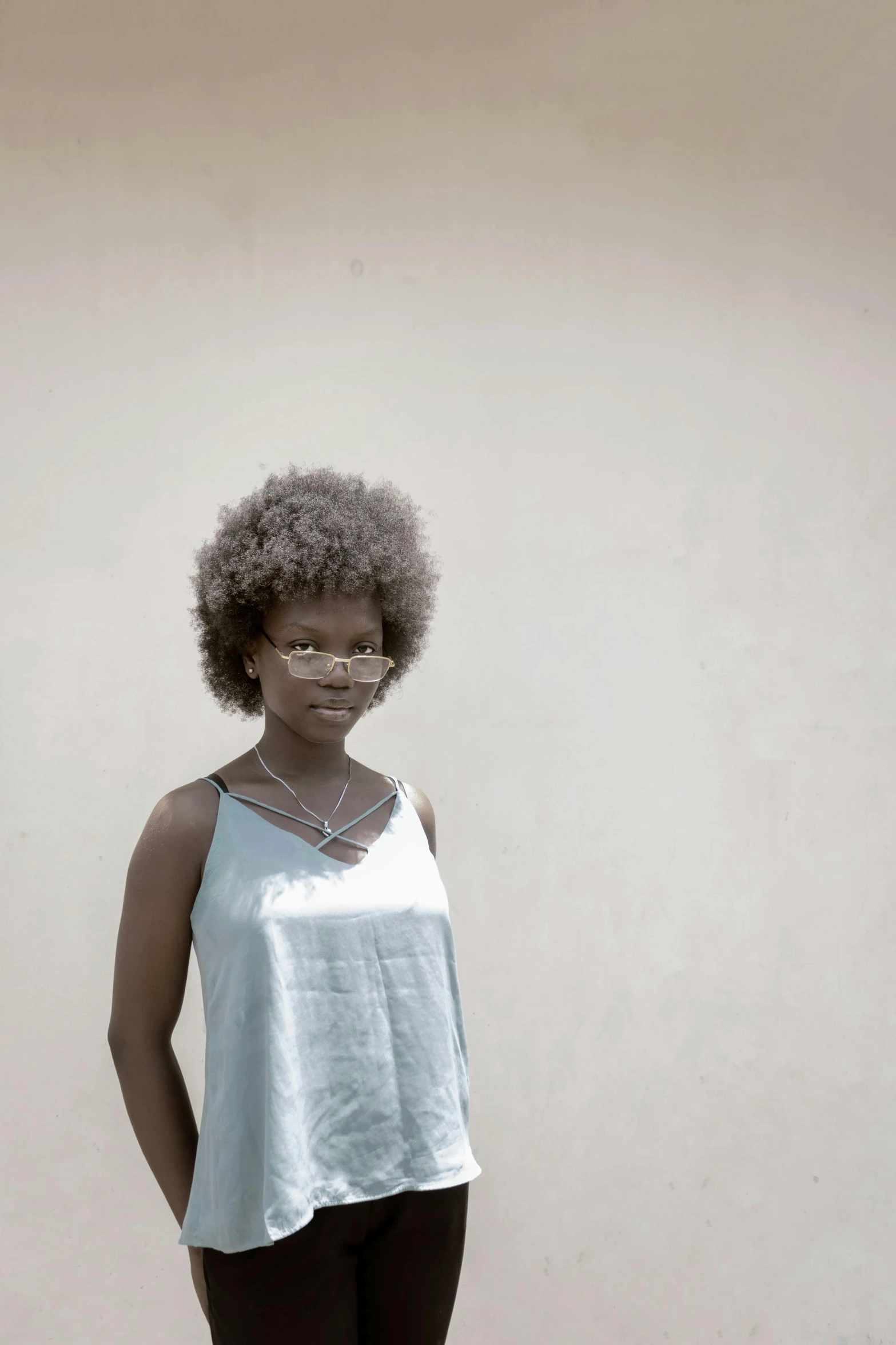 a black woman with an afro haircut wearing glasses and posing in front of a wall