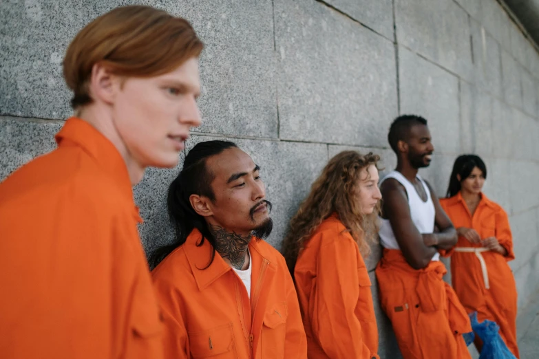 the men in orange uniforms are lined up against the wall