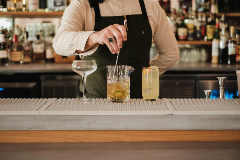 a bartender in an apron stands behind the bar as it prepares a drink