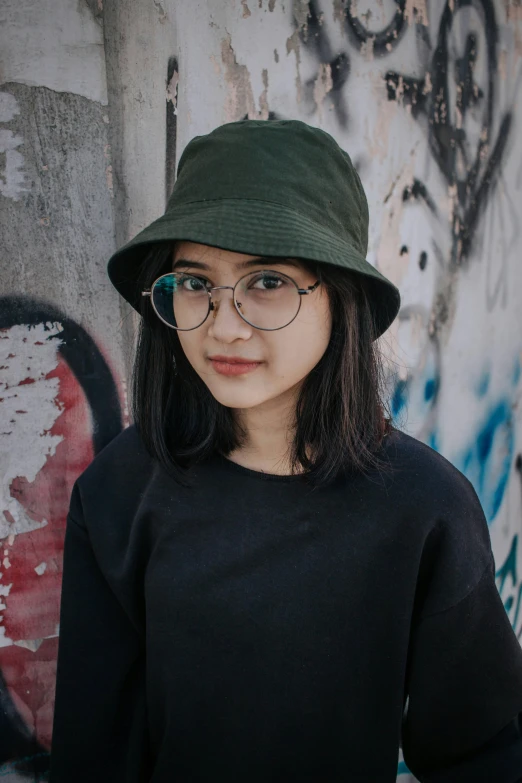 a person wearing glasses and a hat next to a wall