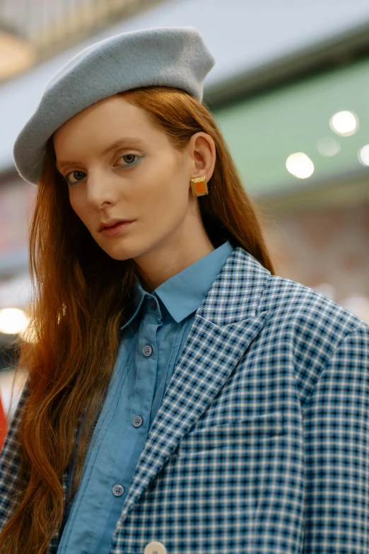 a woman with red hair wears a blue plaid jacket and hat