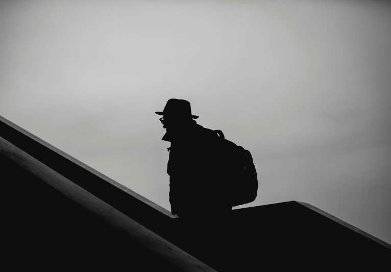 the silhouette of a person in a hat and jacket on an escalator