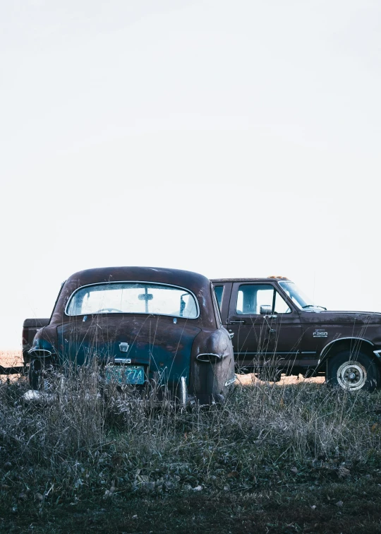 two old cars are standing in a field