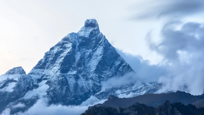 clouds hovering over the top of a snowy mountain