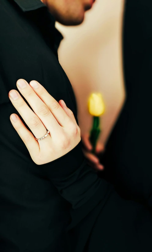 a person wearing a gold ring holds a yellow rose