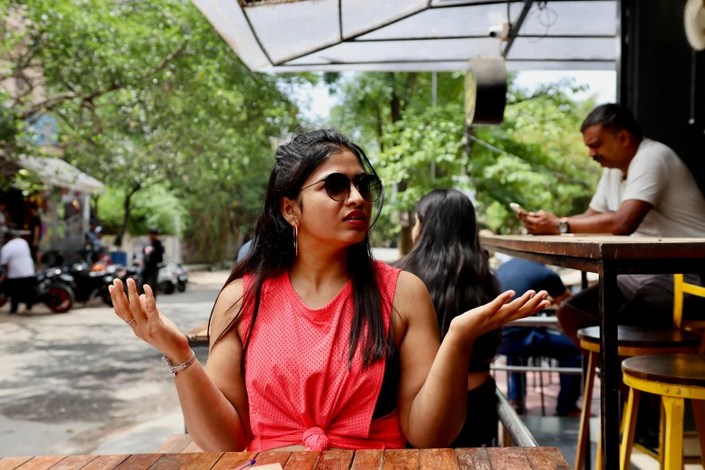 a woman wearing sunglasses sitting at a table holding a cigarette