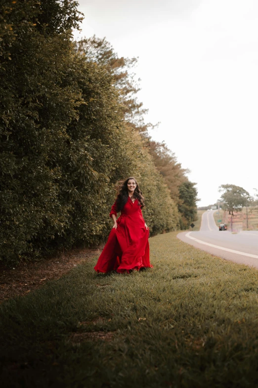 a girl in a red dress walking on the side of a road