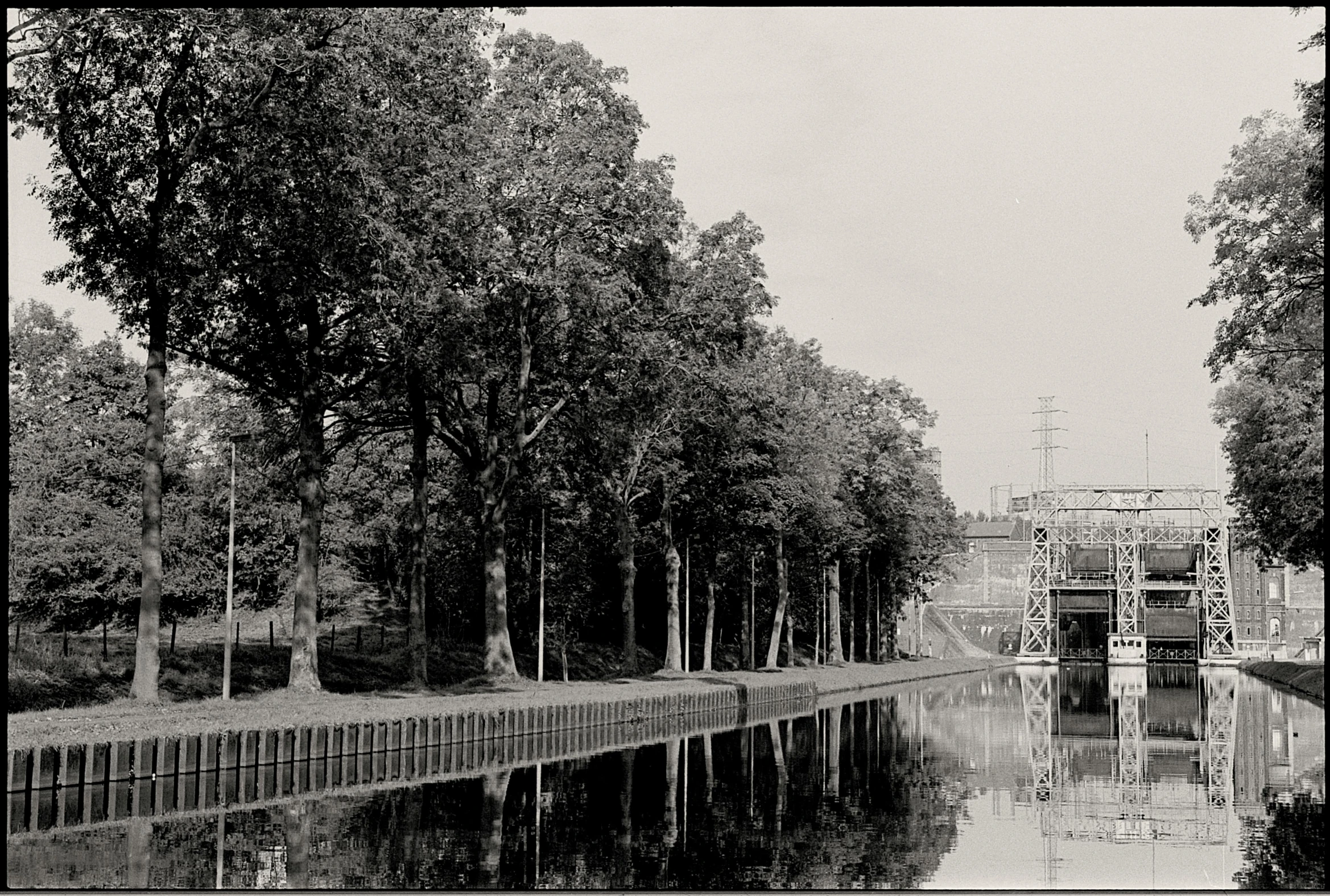 a water front with some trees in the foreground and a fence across the river