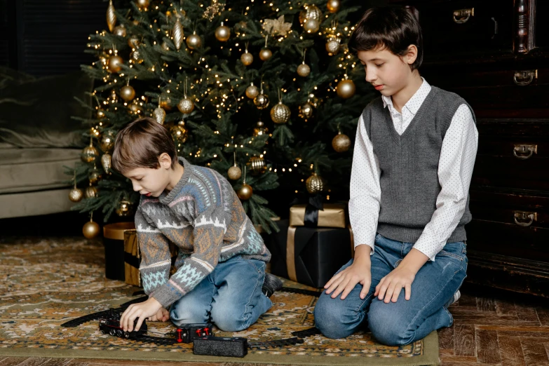 two small children sit near a christmas tree playing with a train