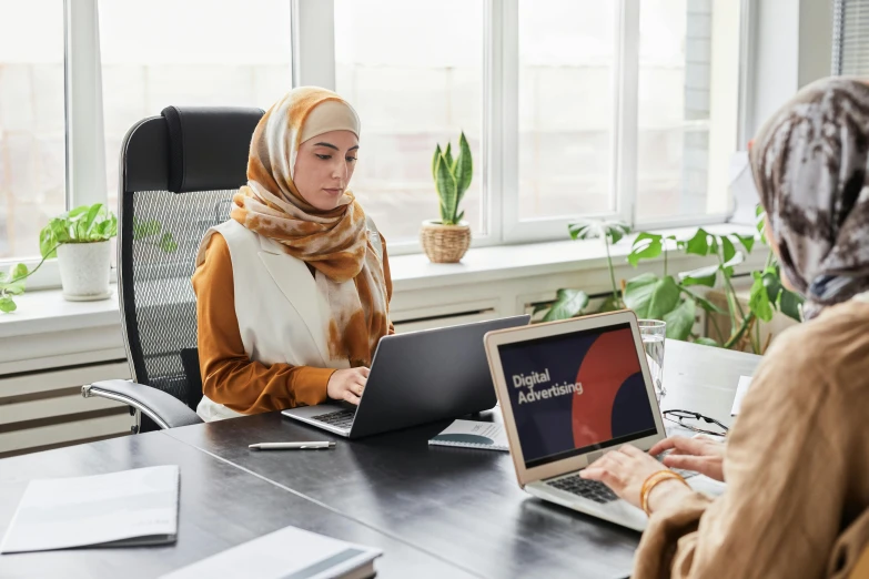 two women in scarves are looking at computers