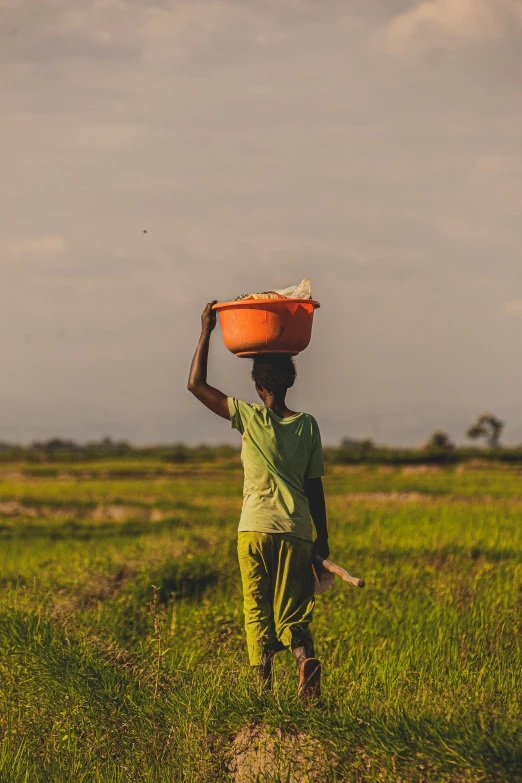 man carrying bowl on his head while walking across a field