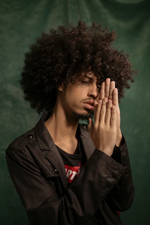 a man with a afro is wearing a black shirt and holding his hands up to their face