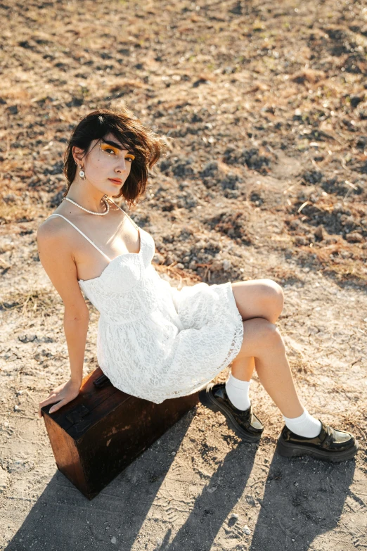 a woman posing in a dress and boots sitting in the sand