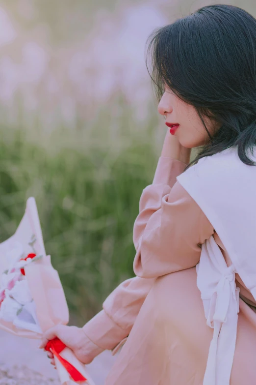 a young woman sitting in the grass looking down at soing