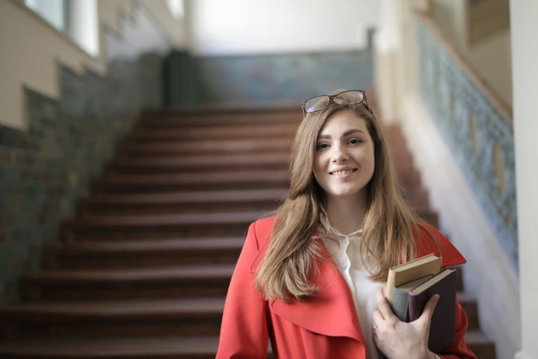 a smiling woman holding an open book near a stair case