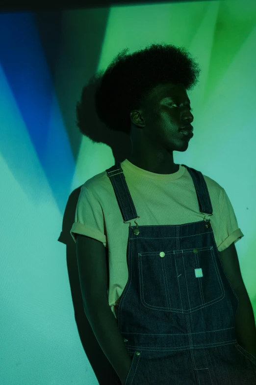 a black person wearing overalls standing in front of a green screen