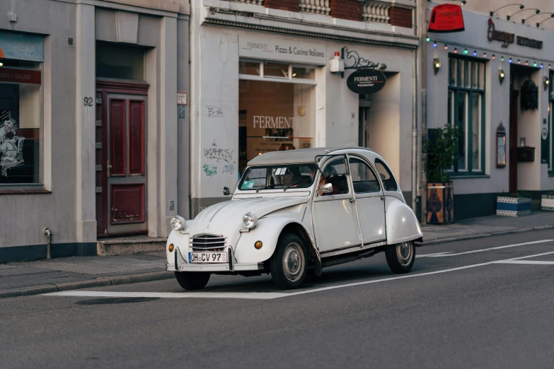 an old white car driving down a street