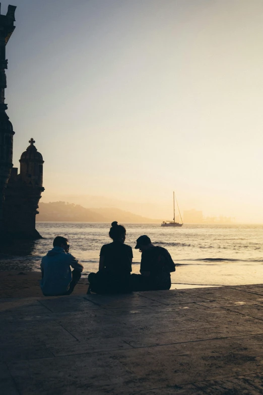 three people sit on the sand by the water