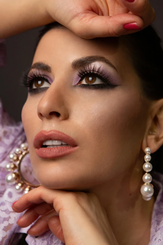 a woman with purple eye makeup holding her hand up to her face