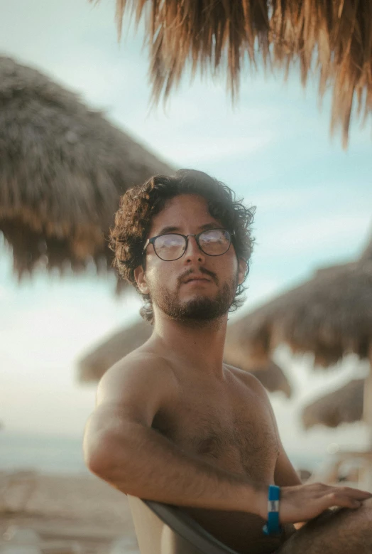 a shirtless man with  on standing under a straw umbrella