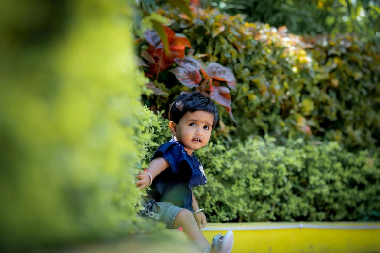 a young child wearing shorts and a blue vest walking next to bushes