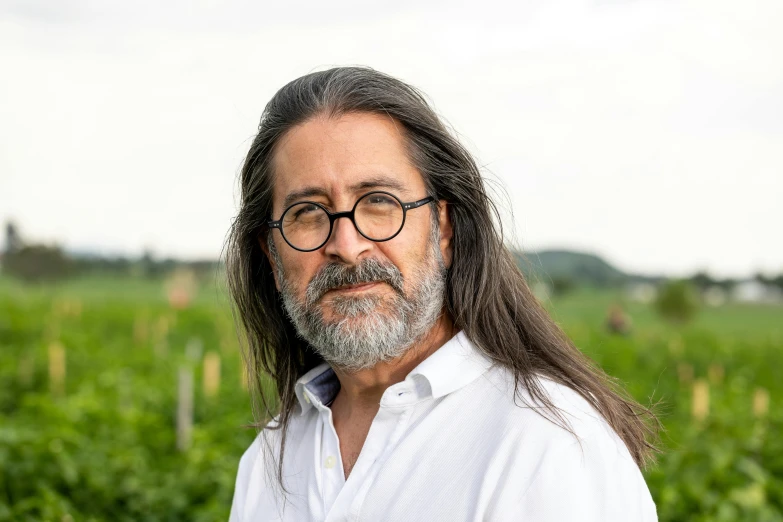 a man with long hair and glasses is standing in a grassy area