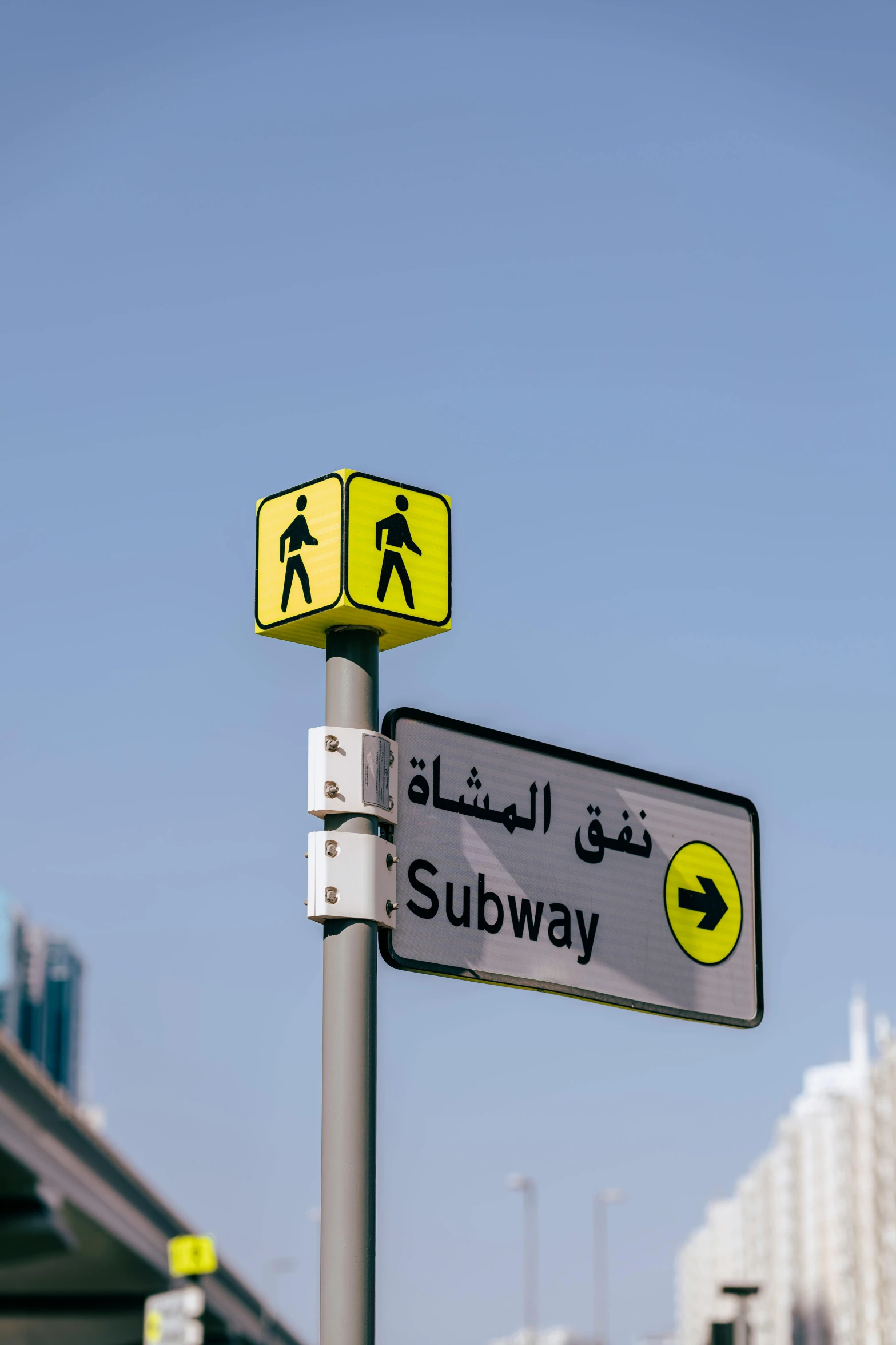 two signs on a light pole with the words subway written in arabic and a yellow arrow pointing left