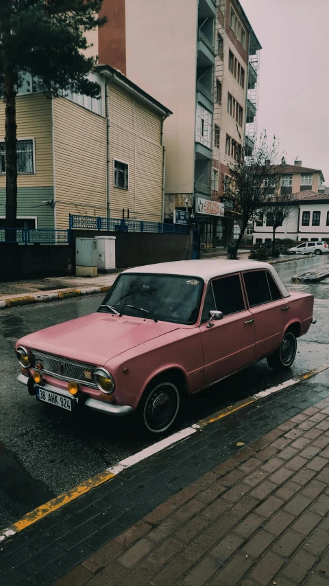 a pink and white car sitting in the rain on a street