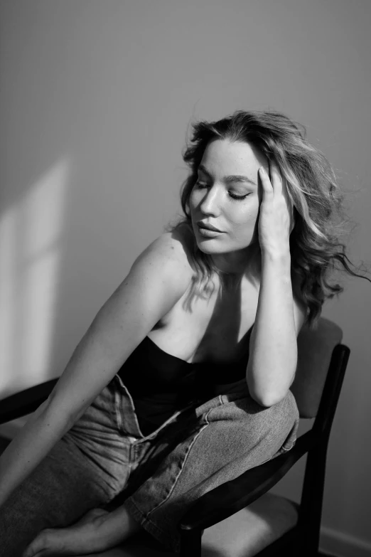 a beautiful young woman sitting in a chair while holding her hand to her head