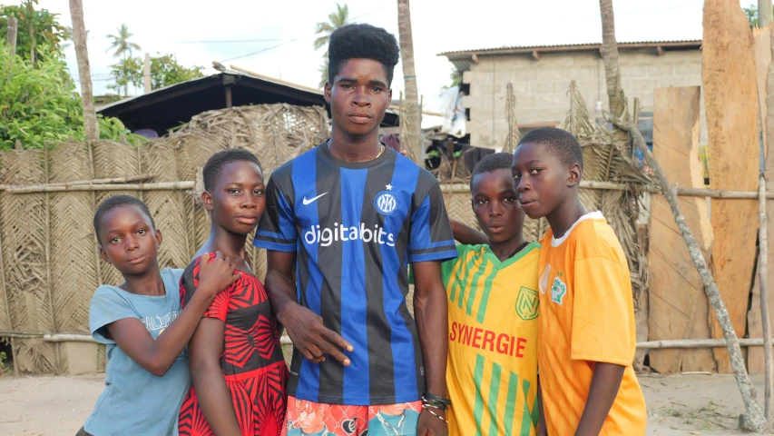 a group of boys and one girl posing in front of some huts