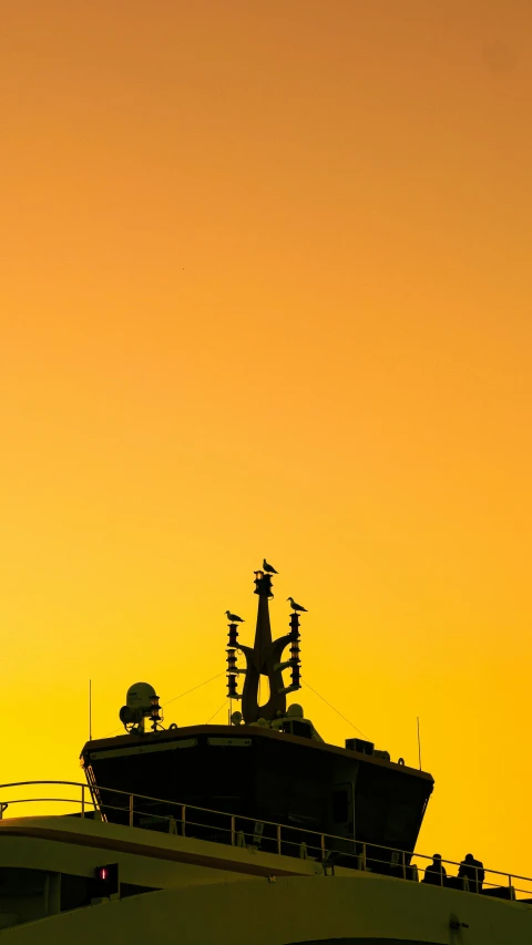 the bow end of a large white ship in silhouette against a golden sky