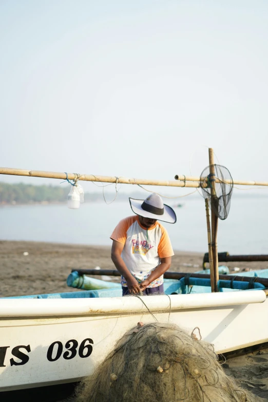 an old man stands beside a row boat on the beach