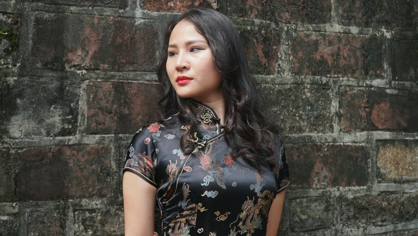 a woman standing near a wall in front of a brick wall