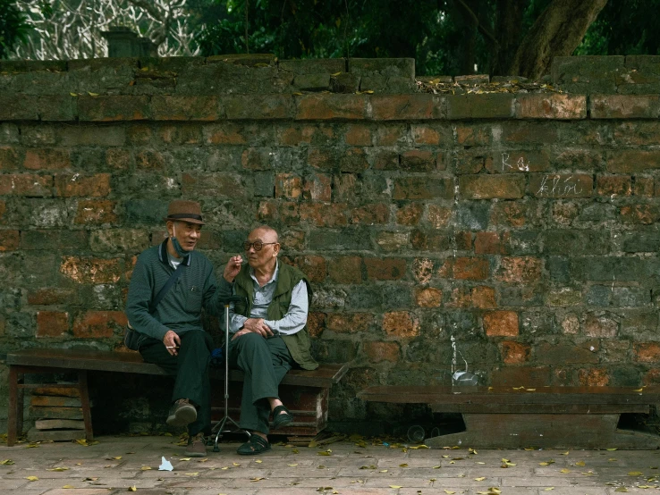 two older people are sitting next to a brick wall