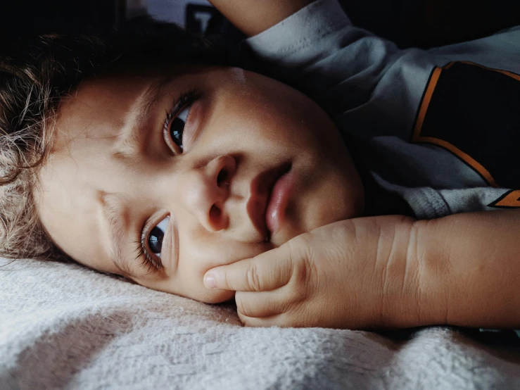 the child is laying down with his arm under the pillows