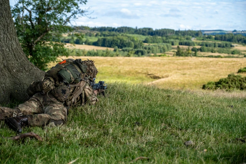 a hunter with a rifle is hiding under a tree