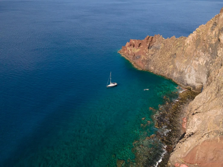 a small boat is in blue water between a cliff