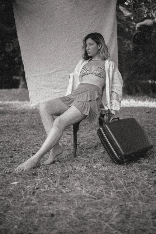 woman sitting in a chair on grass with luggage