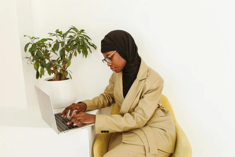 a woman is sitting in a yellow chair using a laptop