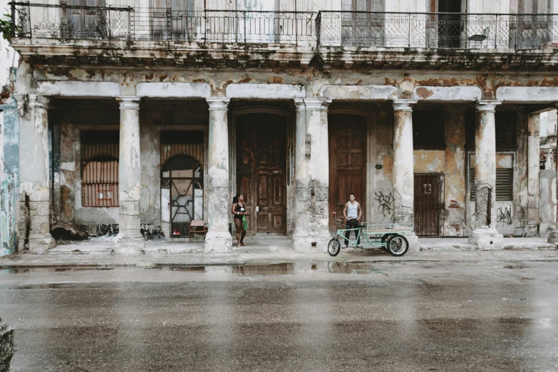 a man stands next to his bike outside a rundown building